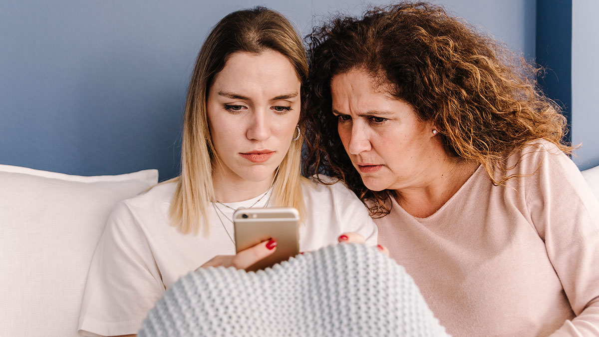 Two women looking at a phone with concerned expressions, hinting at a vacation rift involving sister and friend conflict.