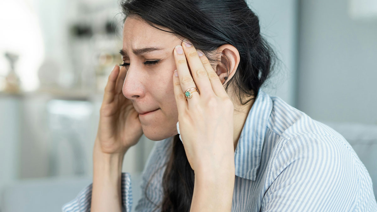 Stressed woman holding temples, upset about getting fired, reflecting the emotional impact of job loss and friendship issues.