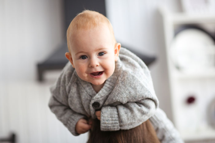 Smiling baby in a gray sweater being held, illustrating the theme of woman choosing to be a single mom and babysitting challenges.