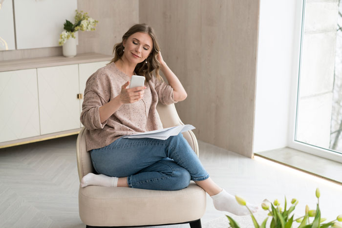 Woman sitting relaxed in chair, checking phone and holding papers, discovering contractors quoting jobs for home remodel plans. Woman sitting relaxed in chair, checking phone and holding papers, discovering contractors quoting jobs for home remodel plans.