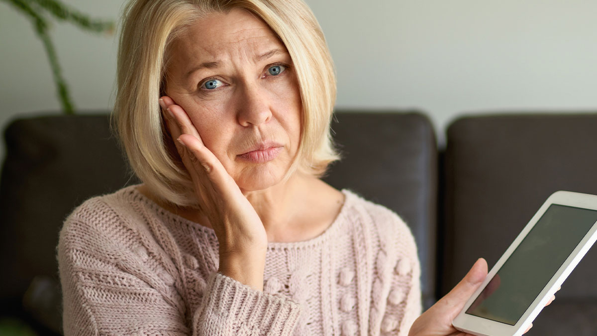 Middle-aged woman looking upset while holding a tablet, reflecting on rude comment about momu2019s friend.
