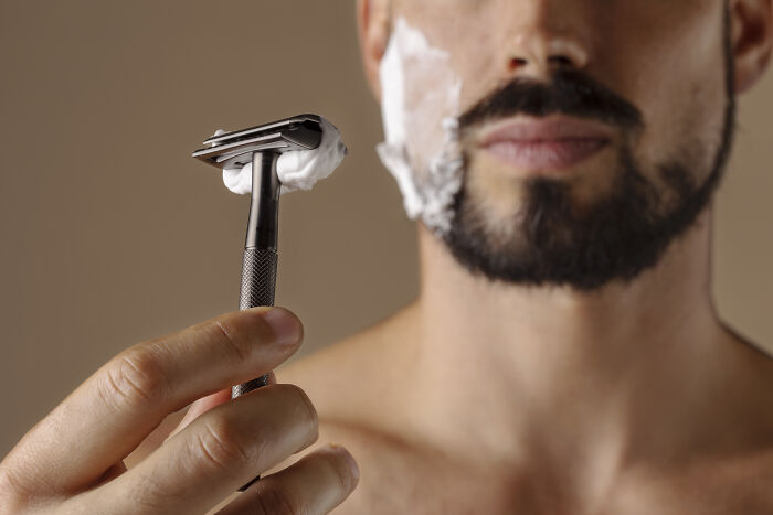Close-up of a man holding a razor with shaving cream on his face, illustrating truckers share craziest things seen.