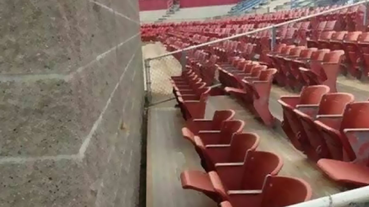 Empty stadium seats blocked by a metal fence against a wall, showing an engineering design mistake.