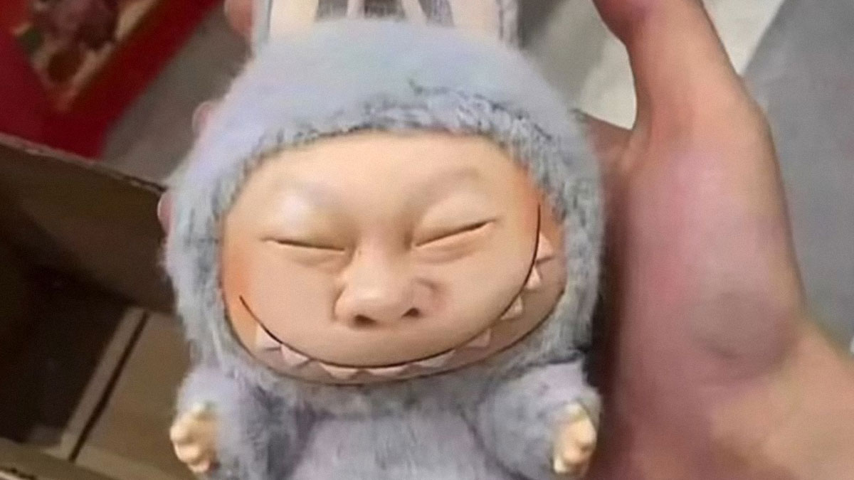 Close-up of a creepy Labubus fake doll with a distorted smiling face, held in a person's hand.