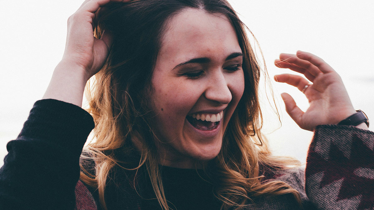 Young woman laughing joyfully outdoors, capturing the spirit of hilarious posts shared with your circle of idiots.