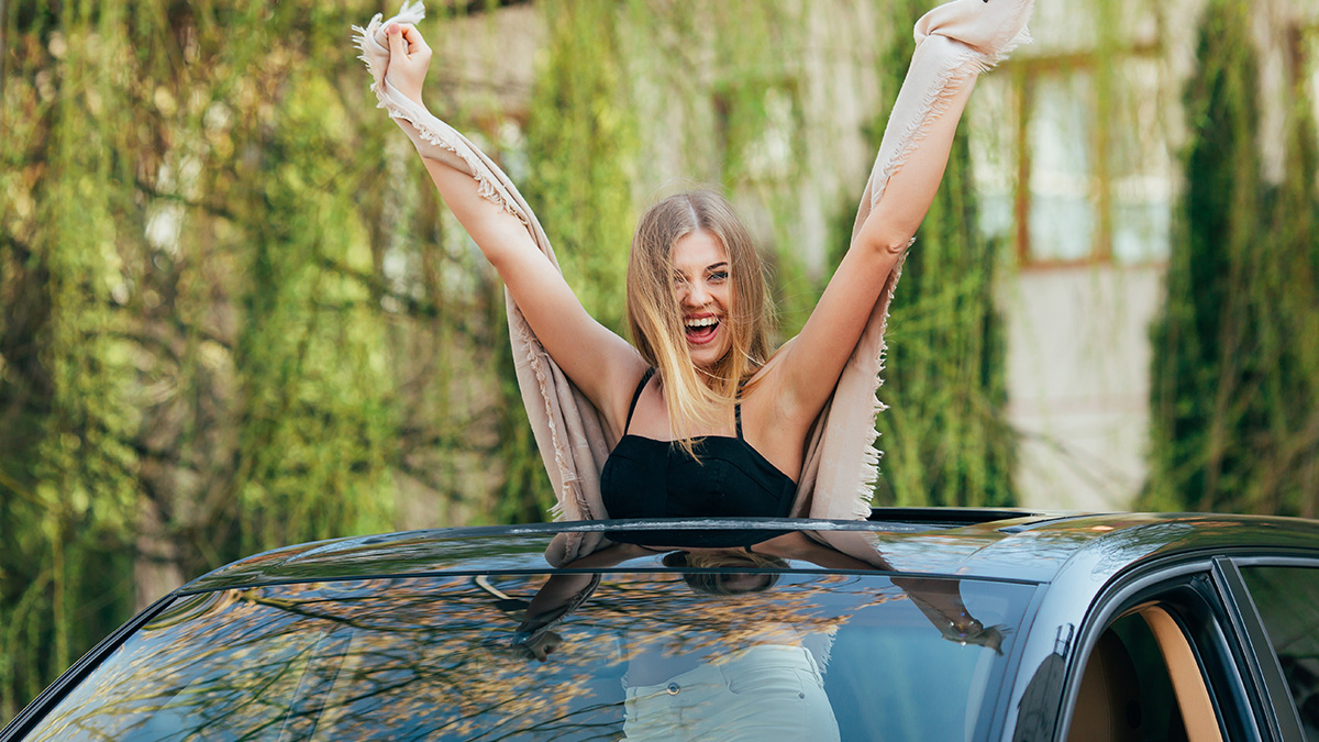 Woman joyfully leaning out of car sunroof with arms raised, symbolizing lawyers and defendants failing miserably in court struggles