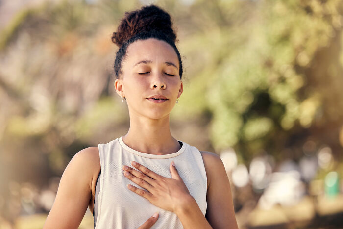 Young woman outdoors with eyes closed and hand on chest expressing calm gratitude, reflecting Gen Z compliment culture.