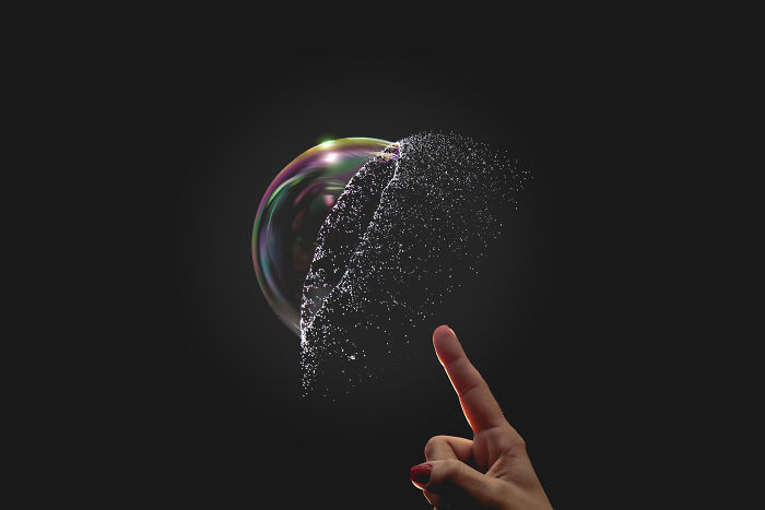 Close-up of a finger popping a soap bubble, symbolizing creative and outlandish ways Gen Z hand out compliments.