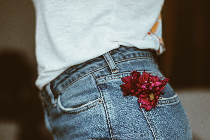 Close-up of person wearing jeans with red flowers tucked in pocket, illustrating Gen Z ways to hand out compliments.