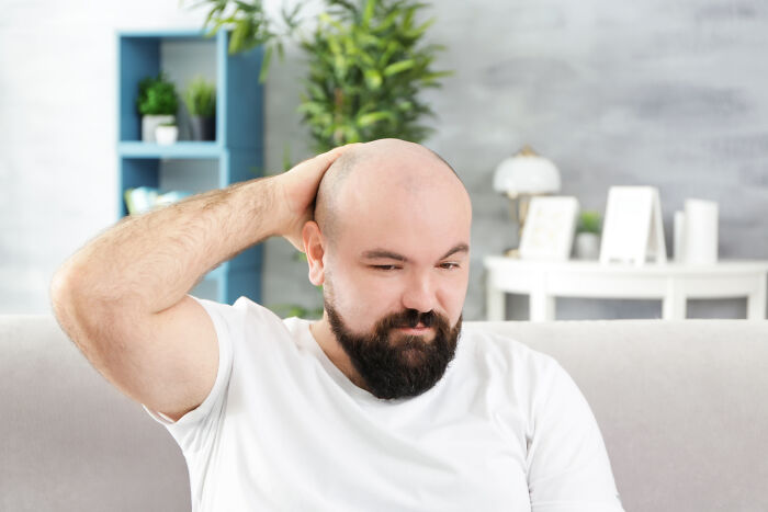 Bearded man in a white shirt sitting on a couch, looking thoughtful, relating to Gen Z outlandish compliments trends.