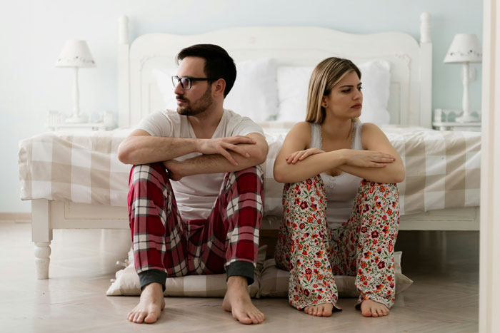 Couple sitting on bedroom floor looking away from each other, showing tension after wife’s weird quirk made traveling difficult. Couple sitting on bedroom floor looking away from each other, showing tension after wife’s weird quirk made traveling difficult.