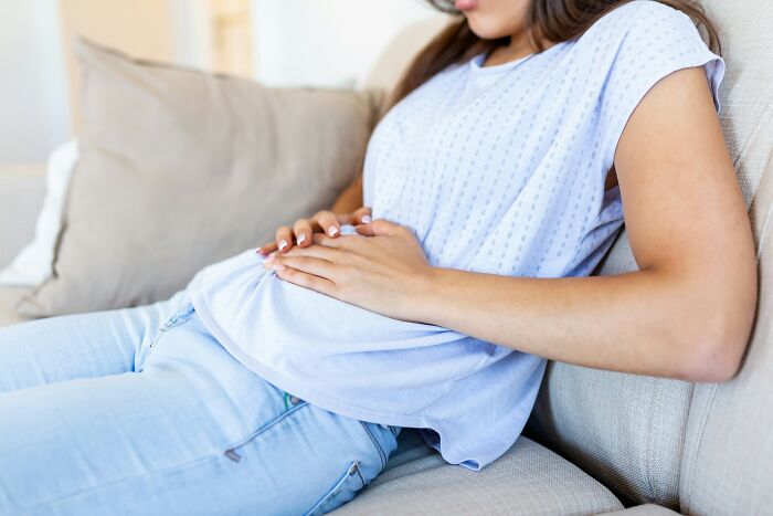 Pregnant woman in casual clothes sitting on a couch holding her belly, illustrating common lies proven false over time.