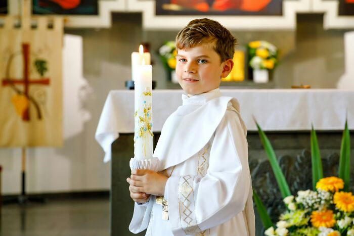 Young boy in white robe holding decorated candle during religious ceremony, illustrating outrageous student names concept.