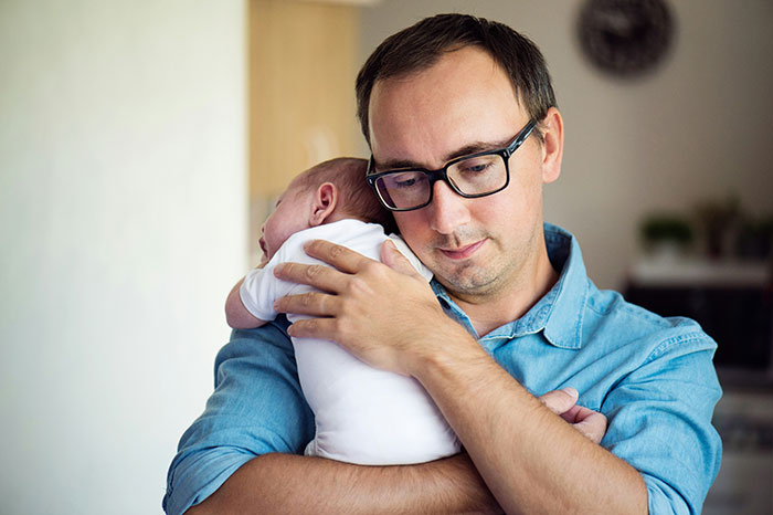 Man wearing glasses holding a newborn baby, illustrating bio dad refuse babysit family drama concept.