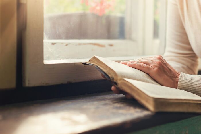 Person reading an old open Bible by a window, addressing myths about Jesus writing the Bible.