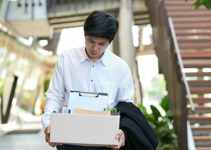 Young man holding box of personal items, looking down after leaving office, illustrating stories of revenge on their bosses.