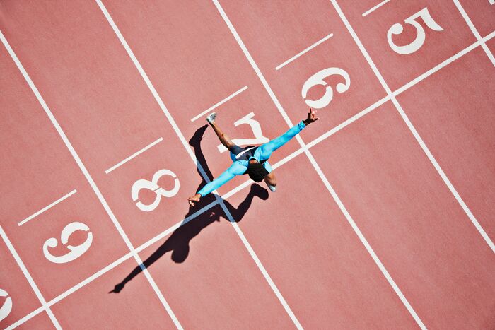 Runner in bright blue outfit crossing finish line on track, illustrating energy and pace related to student names topic.