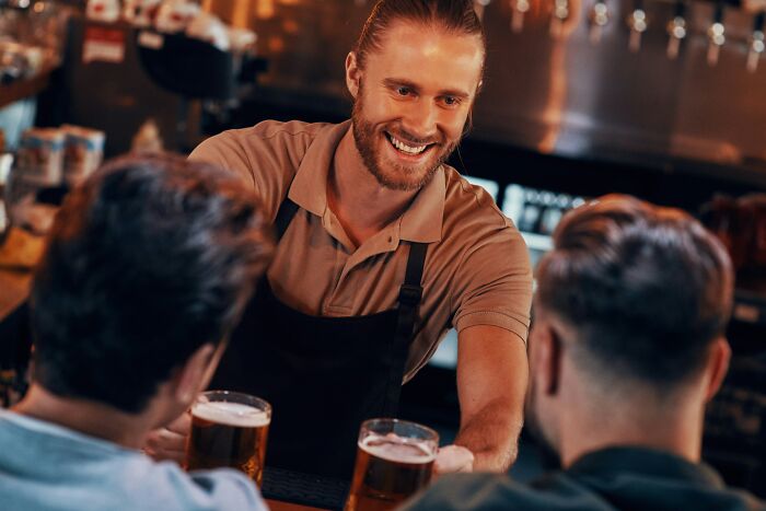 Smiling bartender serving beer to two customers at a bar, illustrating outrageous student names shared by a teacher.