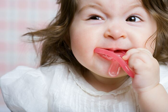 Baby chewing on a red teething toy, illustrating bizarre beliefs people still fall for despite science busting myths.