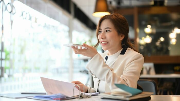 Young woman communicating calmly during a meeting, smiling and holding a smartphone in a modern office setting.
