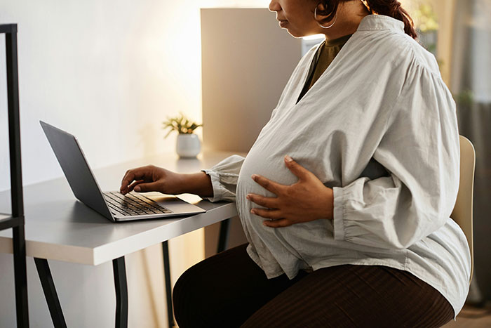 Pregnant woman working on laptop at home, reflecting family conflict and racist switch over babysitting niblings. Pregnant woman working on laptop at home, reflecting family conflict and racist switch over babysitting niblings.