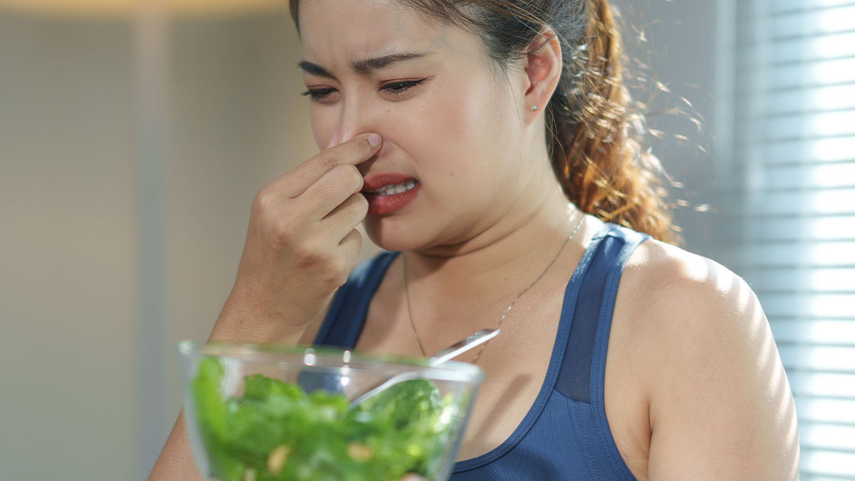 Woman holding a bowl of salad pinching her nose in disgust, reflecting picky eating and food refusal frustration.