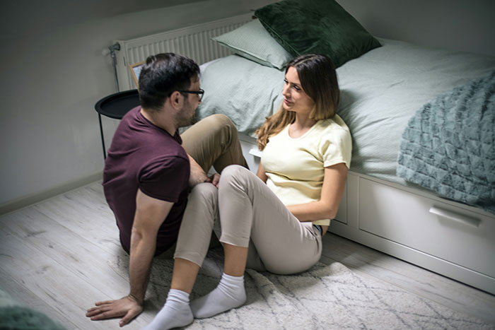 Man and woman sitting on bedroom floor, having a serious conversation about girlfriend not visiting in the mornings. Man and woman sitting on bedroom floor, having a serious conversation about girlfriend not visiting in the mornings.