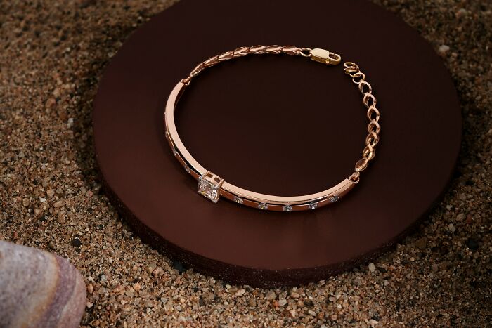 Rose gold bracelet with a central diamond placed on a brown circular platform on a sandy surface, illustrating bizarre beliefs.