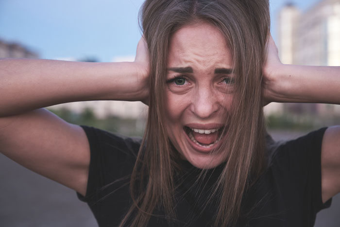 Woman covering ears with hands and screaming outdoors, showing distress related to gold digger holiday friend drama. Woman covering ears with hands and screaming outdoors, showing distress related to gold digger holiday friend drama.