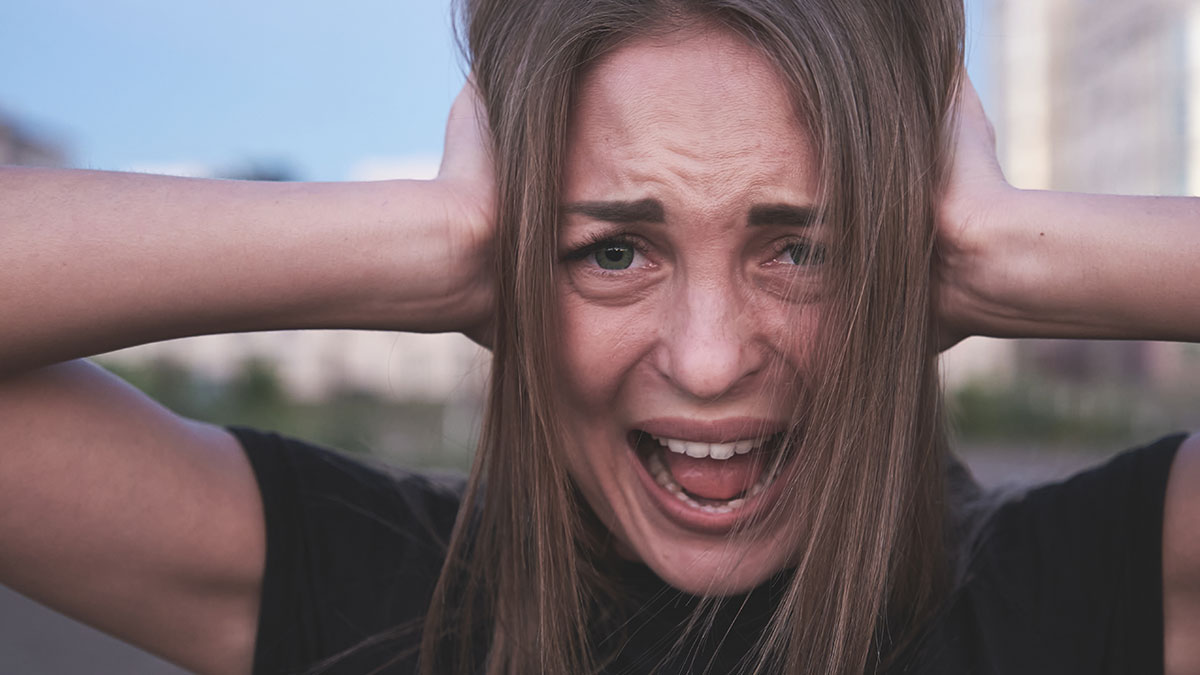 Young woman covering ears and screaming outdoors, showing frustration and anger in a tense moment about a canceled trip.