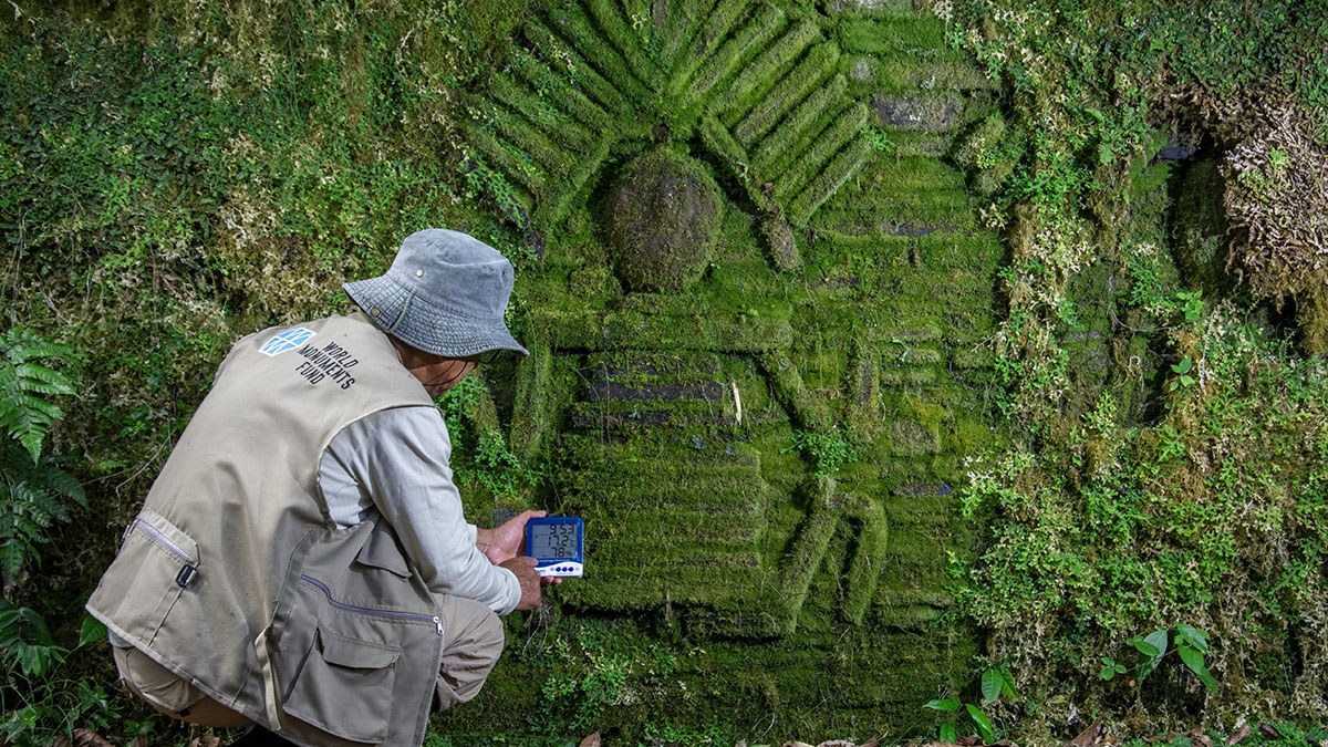 Archaeologist examining moss-covered ancient carved stone structure linked to mysterious ancient civilization in dense forest.