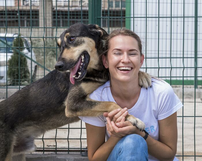 A woman smiling happily with a dog hugging her, showing oddly specific green flags in relationships.