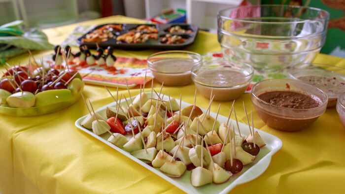 Assorted fruit and snack platters with toothpicks arranged on a table for easy sharing and tasting.