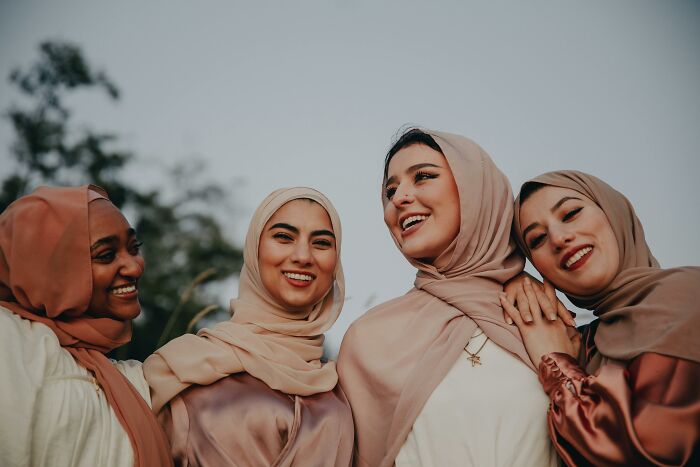 Four diverse women wearing hijabs, smiling and enjoying each other's company, showcasing green flags in friendships.