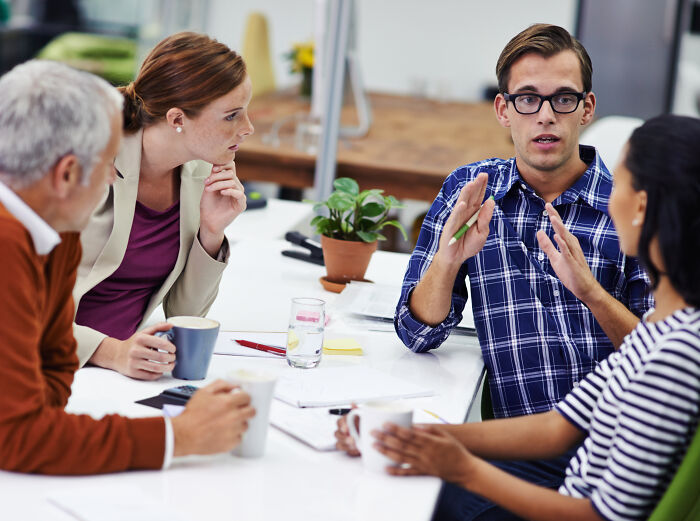 Group of people discussing green flags in relationships during a casual meeting around a white table with coffee cups.