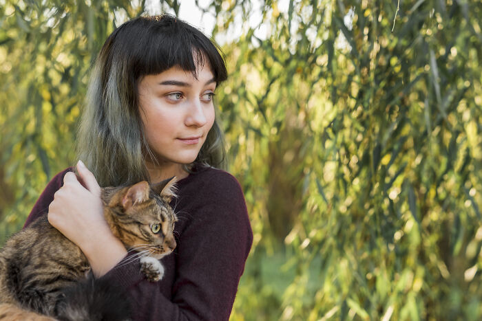 Young woman holding a cat outdoors surrounded by greenery, illustrating oddly specific green flags in relationships.