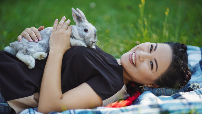 Smiling woman lying on a blanket outdoors holding a gray rabbit, representing oddly specific green flags in relationships.