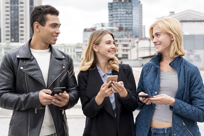 Three friends smiling and chatting outdoors in a city, showing green flags of connection and positive interaction.