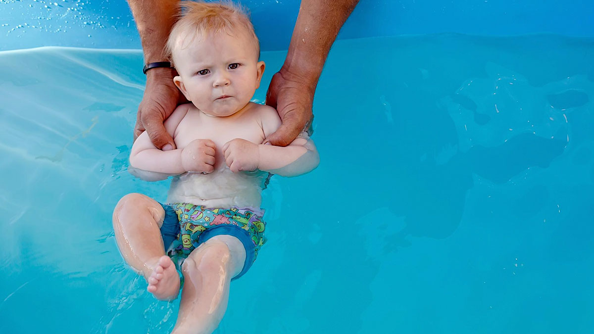 Baby with a serious expression being held in a pool, illustrating unusual things people really did in public.