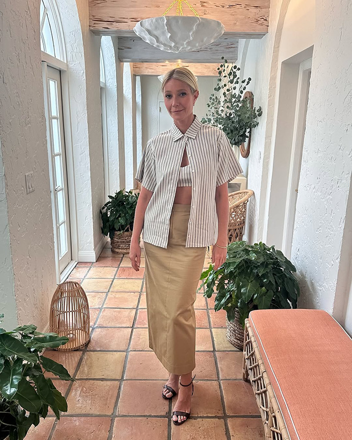 Gwyneth Paltrow standing in a hallway, wearing a striped shirt and beige skirt, before a cooking video on trash handling. Gwyneth Paltrow standing in a hallway, wearing a striped shirt and beige skirt, before a cooking video on trash handling.
