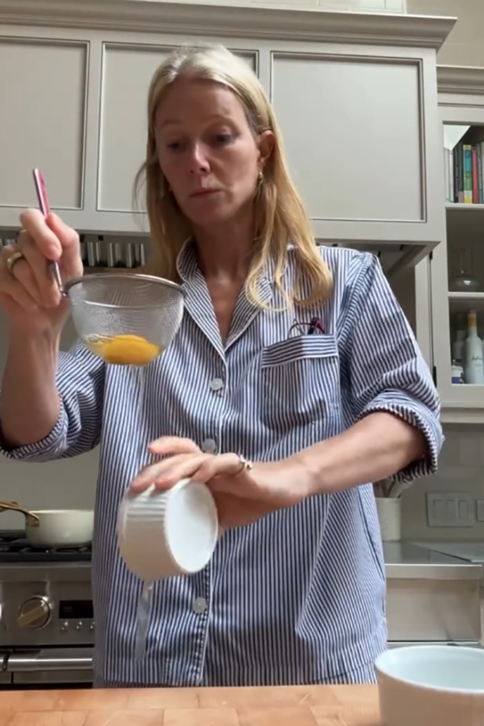 Gwyneth Paltrow in kitchen, pouring liquid while holding a strainer, showing trash-handling skills in cooking video. Gwyneth Paltrow in kitchen, pouring liquid while holding a strainer, showing trash-handling skills in cooking video.