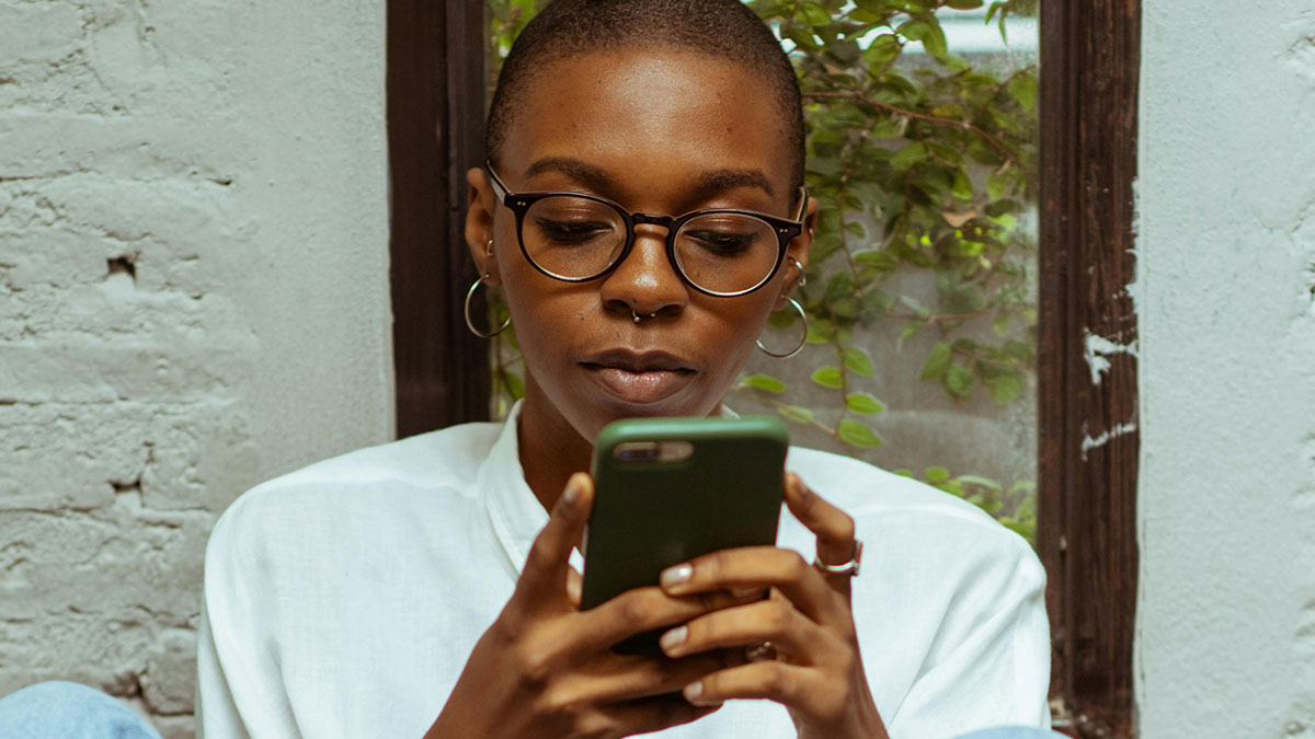 Woman with glasses and hoop earrings looking at phone, reflecting on half-sister wedding invitation and gift expectations.