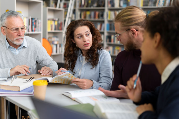 Group of students and adults discussing and studying together around a table in a school hallway or lane setting. Group of students and adults discussing and studying together around a table in a school hallway or lane setting.