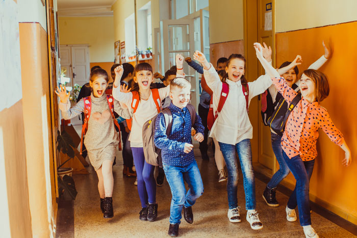 Students with backpacks joyfully running through a brightly lit school hallway filled with laughter and excitement.