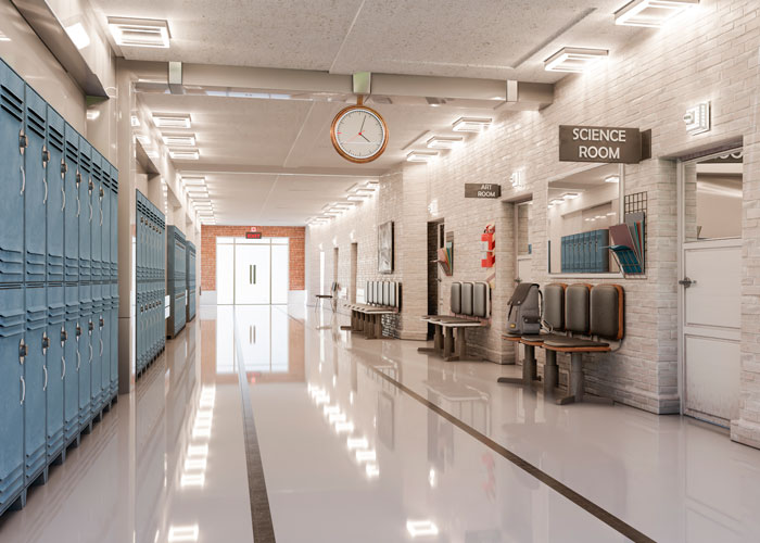 Empty school hallway with lockers and seating lanes leading to classrooms and a large clock overhead.