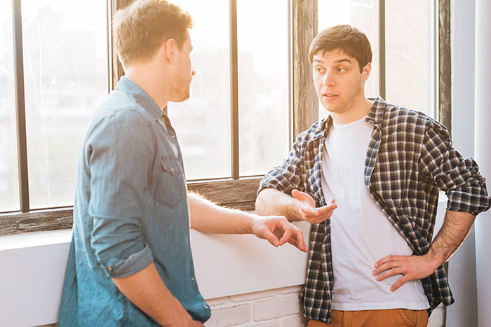 Two men having a tense conversation by a window, depicting family drama involving a bio dad refusing to babysit.