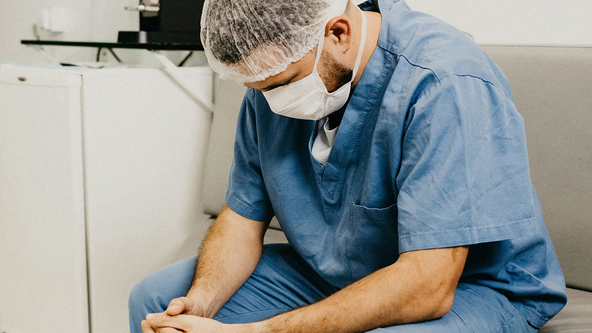 Medical professional in blue scrubs wearing mask and hairnet, showing concern about patients privacy in a clinical setting.