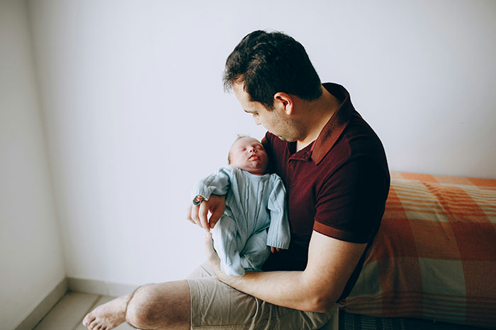 Man holding a newborn baby in a home setting, highlighting bio dad and family drama around babysitting.