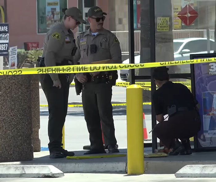 Two sheriffs discussing at a convenience store crime scene with yellow police tape and an investigator crouching nearby. Two sheriffs discussing at a convenience store crime scene with yellow police tape and an investigator crouching nearby.
