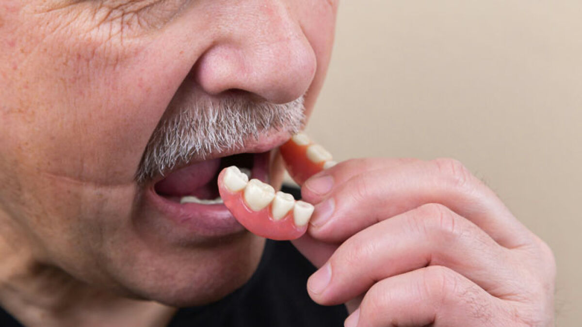 Elderly man holding dentures near mouth, highlighting new tooth regrowth breakthrough that may replace dentures and implants.